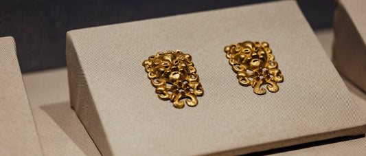 A pair of gold earrings sitting on top of a white box