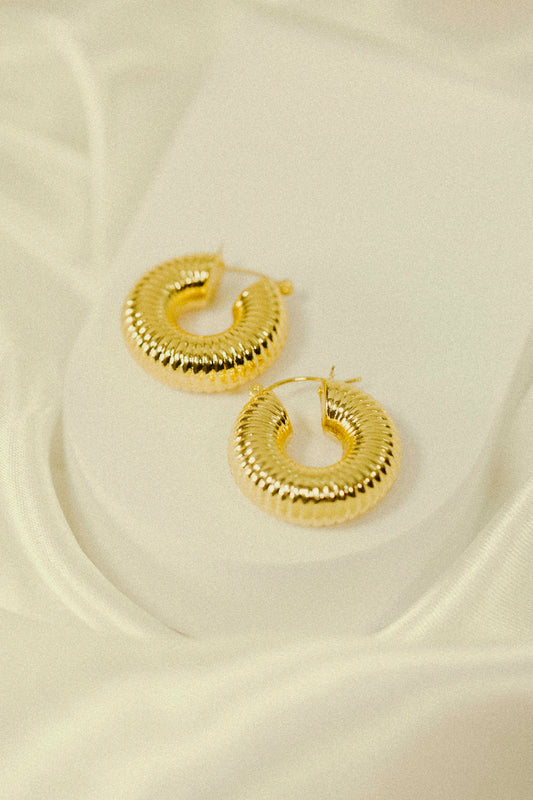 a pair of gold hoop earrings sitting on top of a white sheet