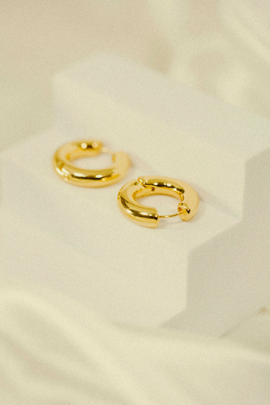 a pair of gold earrings sitting on top of a white surface
