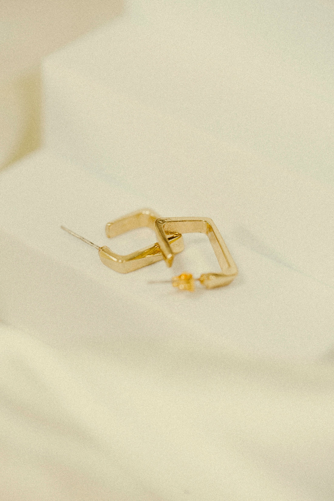 a pair of gold earrings sitting on top of a white sheet