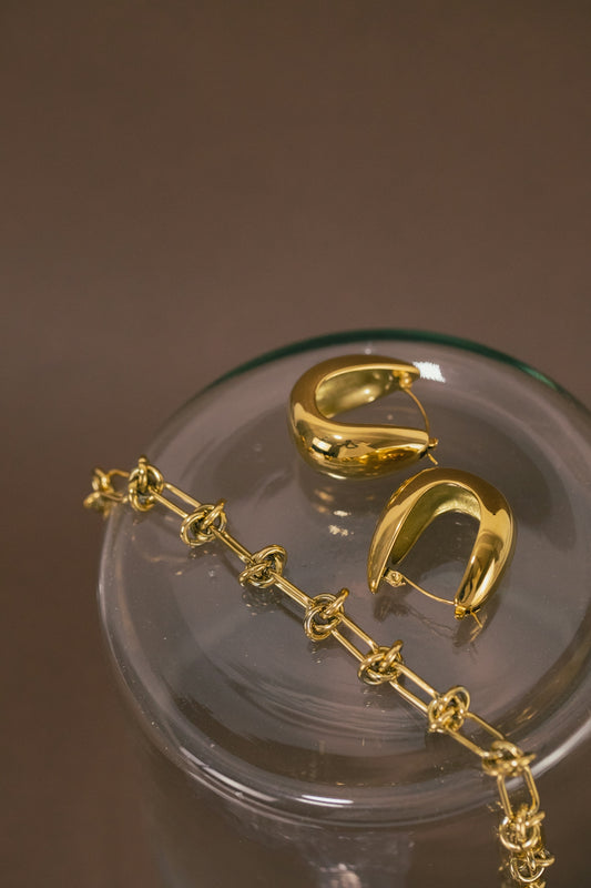 a pair of gold earrings sitting on top of a glass container