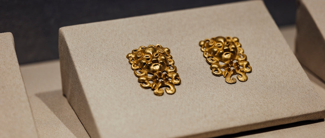 A pair of gold earrings sitting on top of a white box